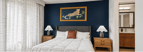 A bedroom with a white bed and a painting of a leopard on the wall.