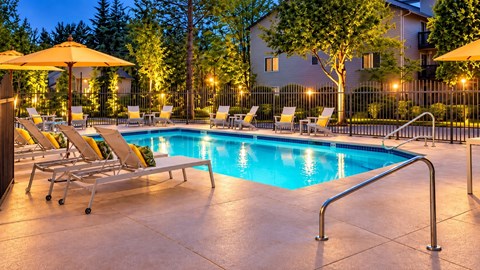 A pool surrounded by chairs and umbrellas at dusk.