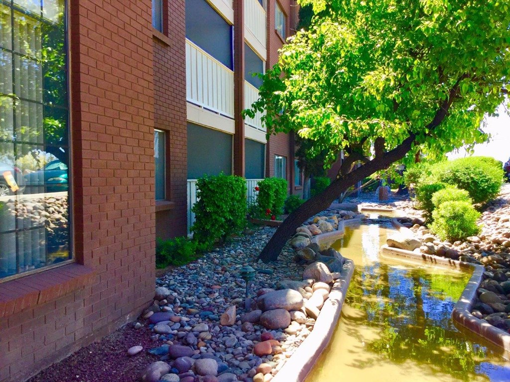 A small stream runs through a landscaped area in front of a brick building.