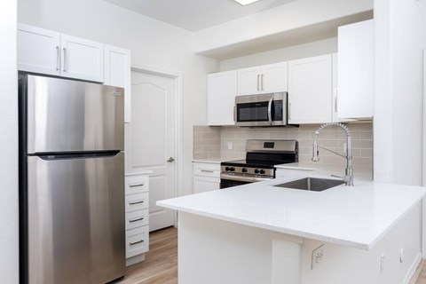 A kitchen with a stainless steel refrigerator, white countertops, and white cabinets.