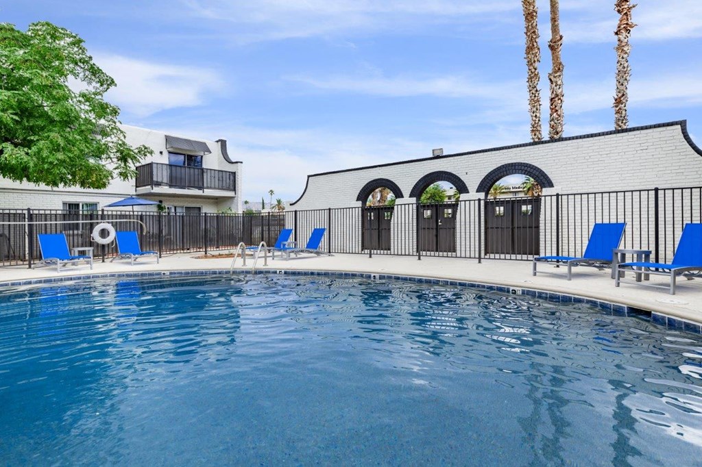 A pool with blue chairs and a black fence.