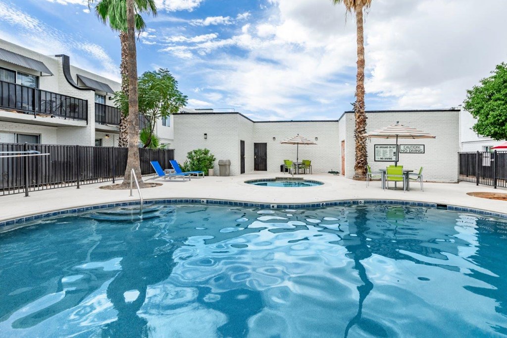 A swimming pool surrounded by a black fence and palm trees.