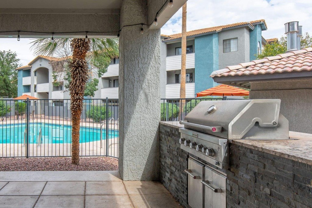 A grill is on a patio next to a pool.