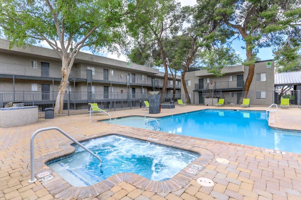 A small pool with a hot tub in the middle of a courtyard surrounded by trees and chairs.