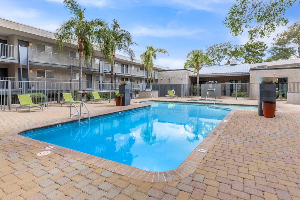 A swimming pool surrounded by a brick patio and palm trees.