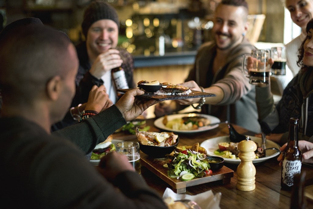 a group of people sitting around a table eating food and drinking beer