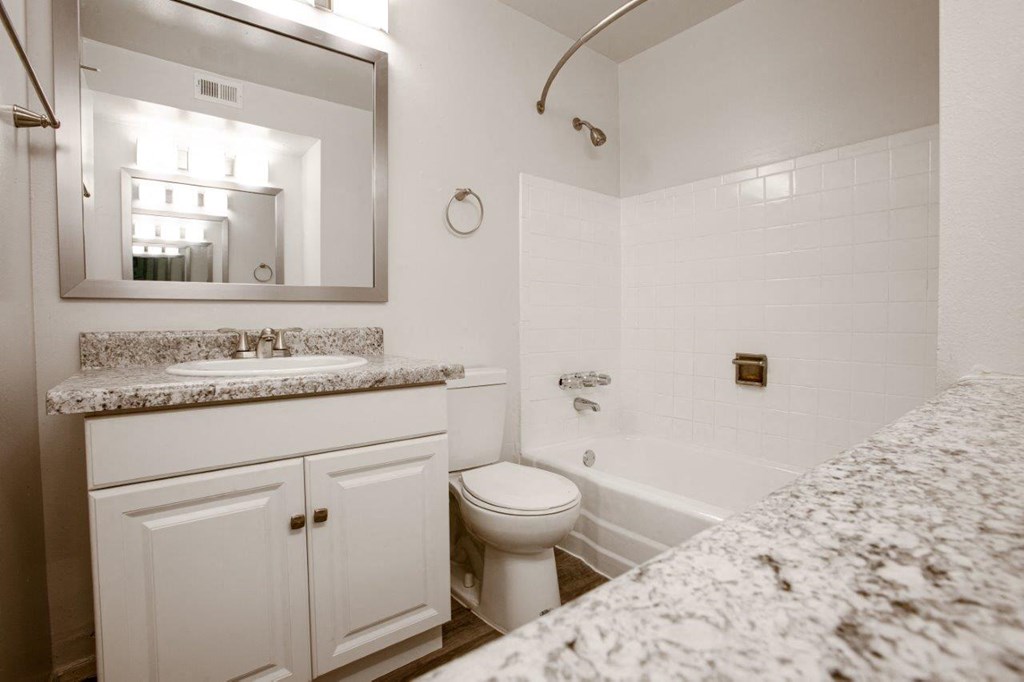 A white bathroom with a marble counter top and a toilet.