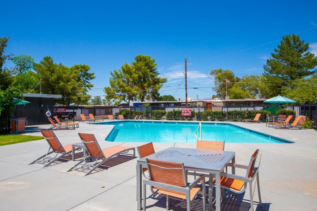 A pool with chairs and a table is surrounded by trees.