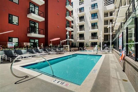 A swimming pool in front of a red building with lounge chairs around it.