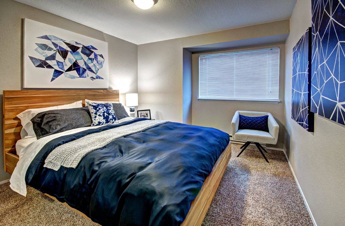 Two-Bedroom Apartments in Silverdale, WA - Ridgetop - Bedroom with Blue Bedding, White Reading Chair, and Wooden Headboard