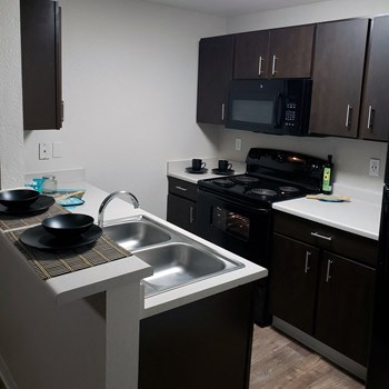 Apartments Kent-Ridgegate Kitchen with Modern Lighting, Matching Black Appliances, Double Sink, and Dark Cabinetry - Photo Gallery 4
