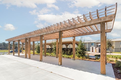 A long wooden pergola extends over a concrete walkway.