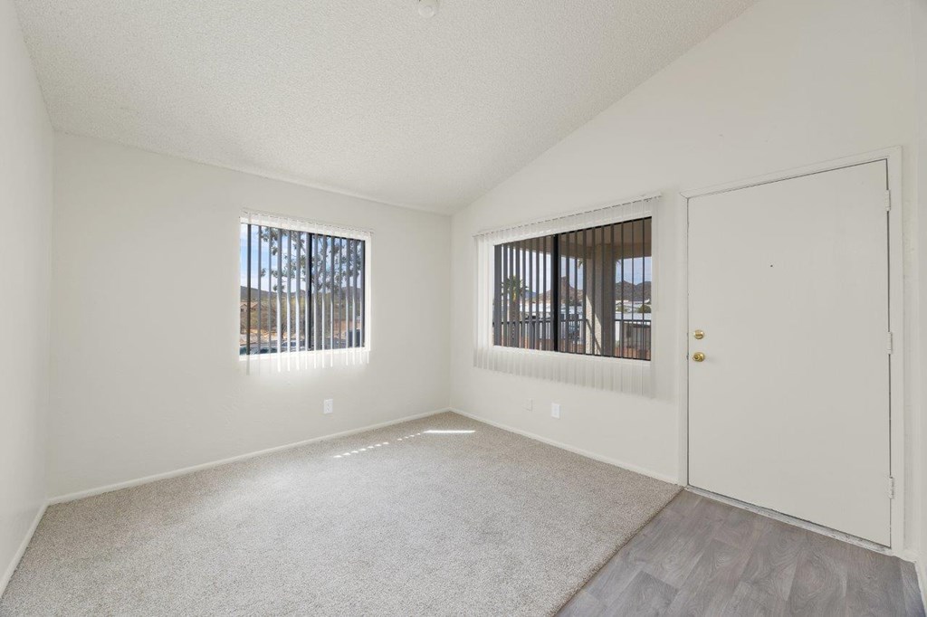 A room with a carpeted floor and two windows with blinds.