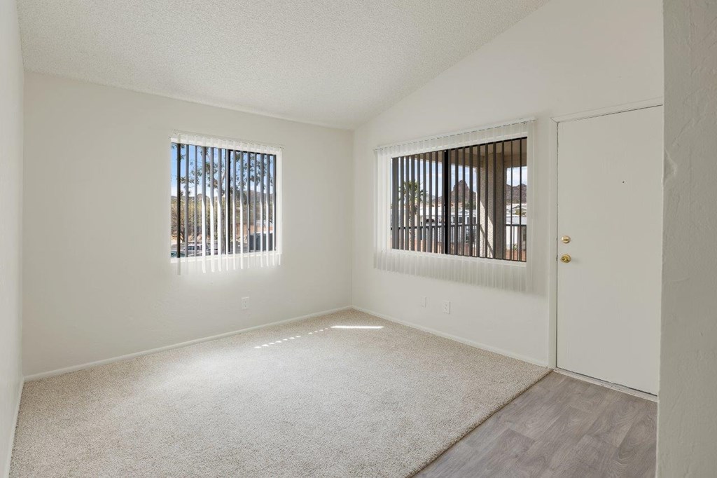 A room with a carpeted floor, two windows with blinds, and a white door.
