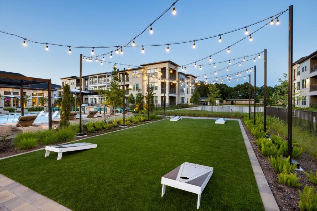 a grassy area with a pool and buildings in the background