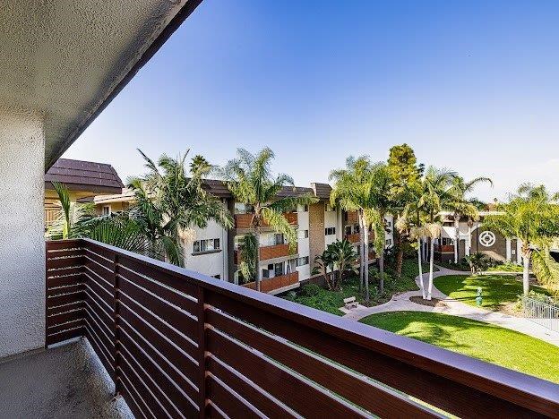 A balcony with a wooden railing overlooks a residential area with houses and palm trees.