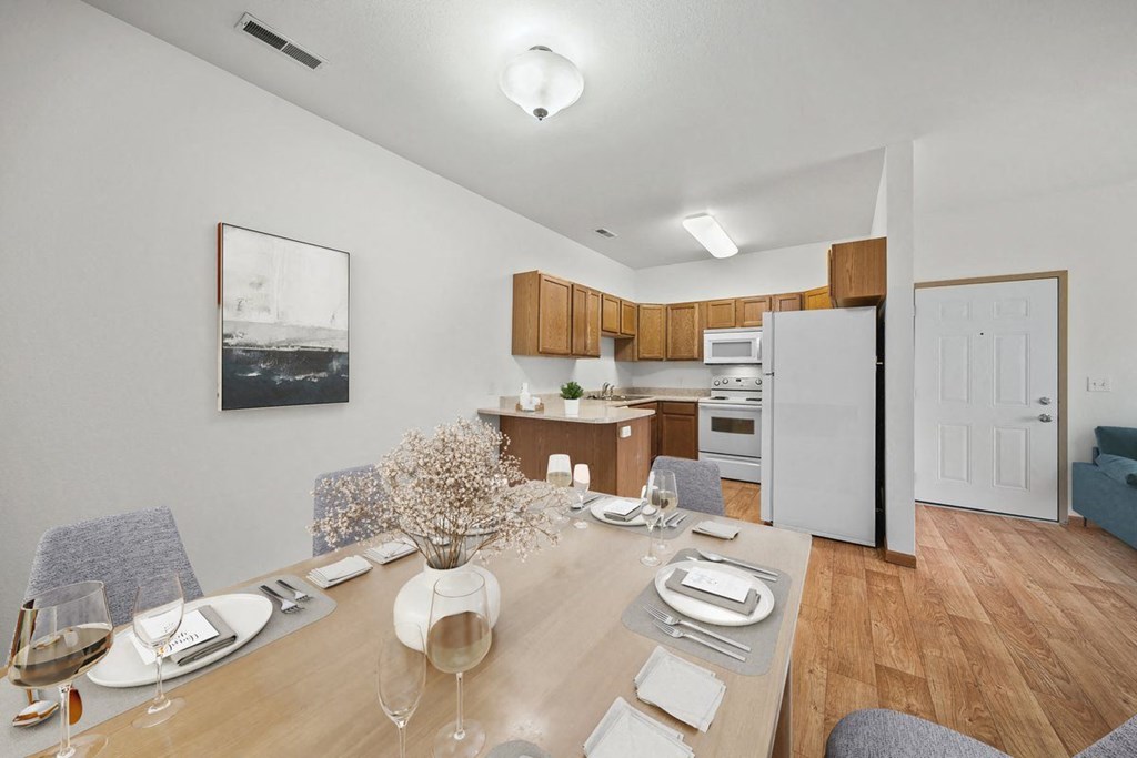 a dining area with a wooden table and chairs and a kitchen in the background