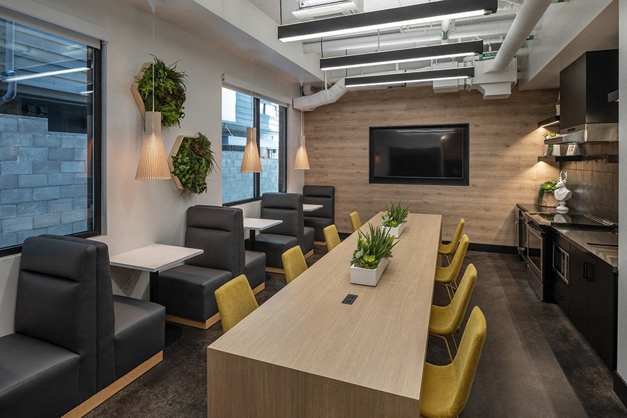 a room with a long table with yellow chairs and black chairs and a television on the wall