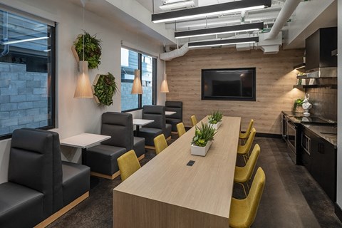 a room with a long table with yellow chairs and black chairs and a television on the wall