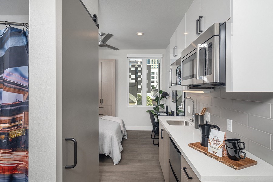 a kitchen with white cabinets and stainless steel appliances and a window with a view of a bedroom
