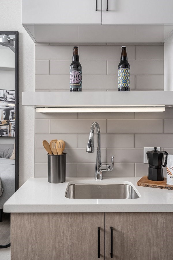 a kitchen sink with white countertops and a white shelf above it with two bottles of beer