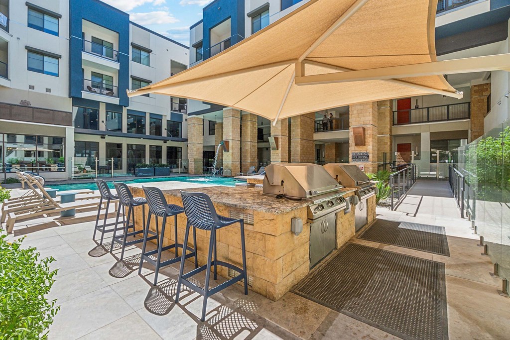 a patio with a grill and a pool with chairs and umbrellas