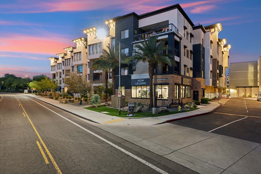 a street view of an apartment building with palm trees at dusk