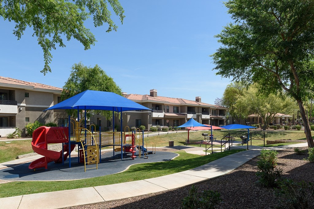 a playground with swings and umbrellas in front of apartments