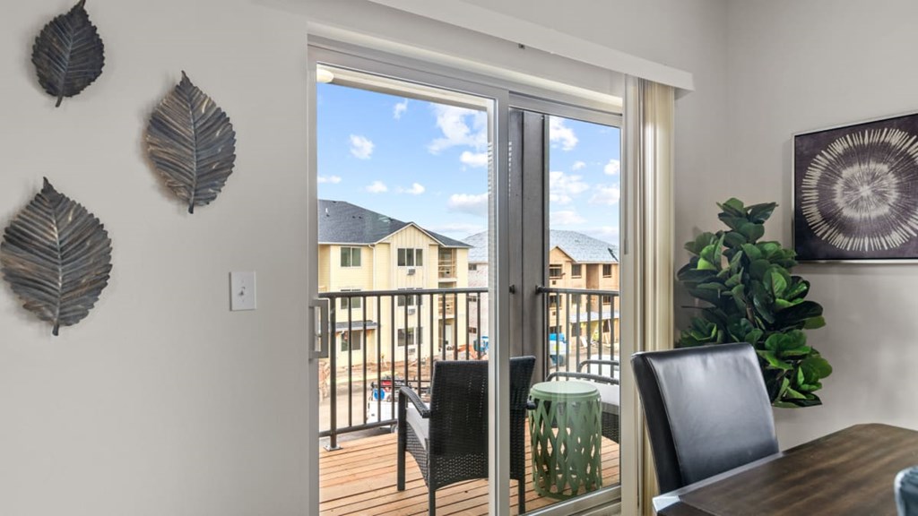 A dining room with a table and chairs and a view of a balcony.