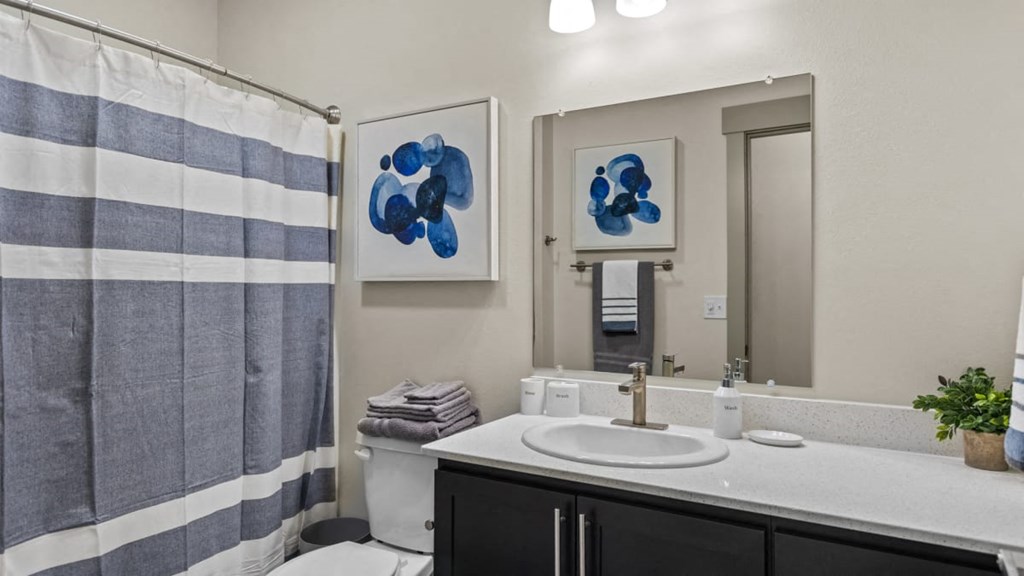 A bathroom with a striped shower curtain and two blue abstract paintings on the wall.