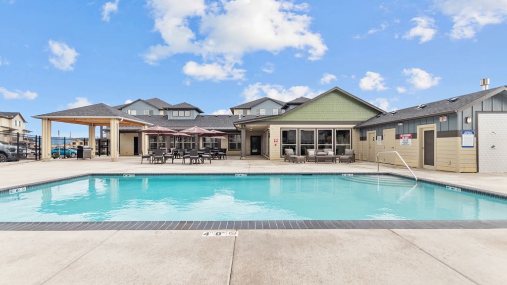 A large swimming pool in front of a building with a covered patio area.