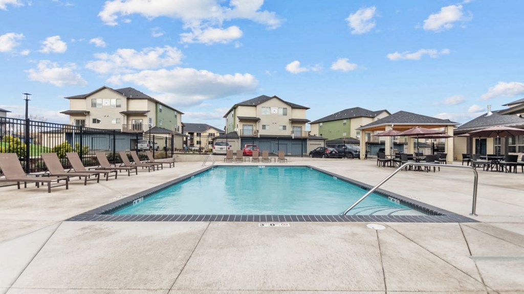 A swimming pool surrounded by lounge chairs and buildings in the background.