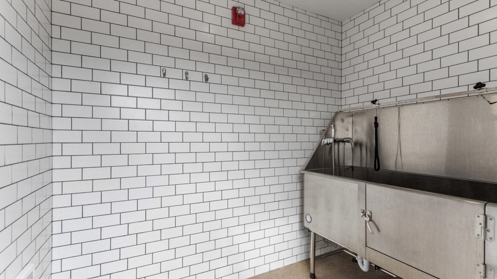 A white tiled wall with a red fire alarm on it.