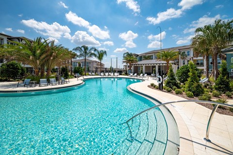 A large swimming pool surrounded by palm trees and a building in the background.
