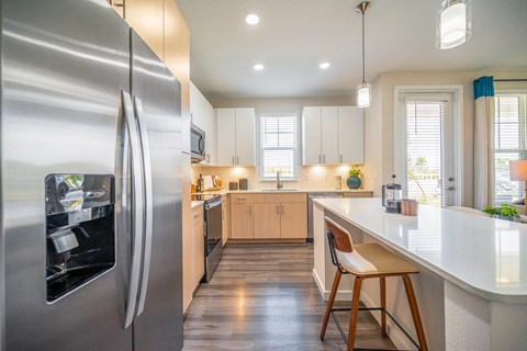 A modern kitchen with a stainless steel refrigerator and wooden flooring.