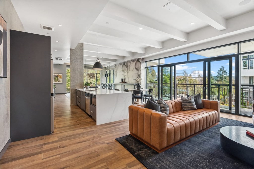 A modern living room with a brown leather sofa and a kitchen in the background at Cru at Willows Apartments, Redmond