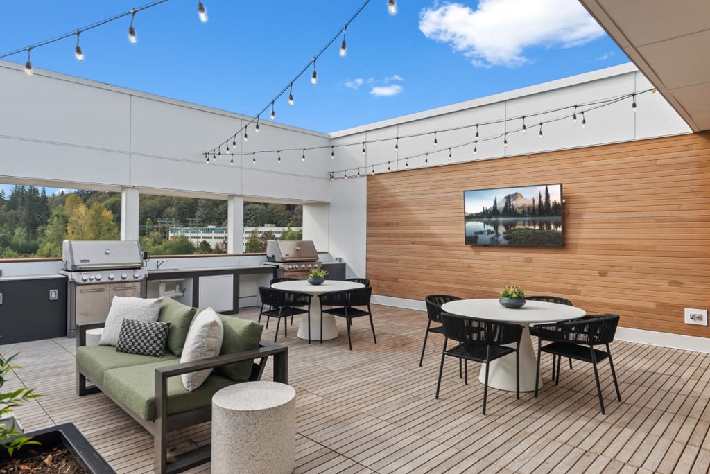 A patio with a table, chairs, and a couch with a view of trees and a house in the distance at Cru at Willows Apartments, Redmond, 98052