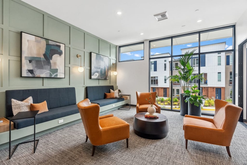 A modern living room with a grey sofa, orange chairs, and a coffee table at Cru at Willows Apartments, Washington