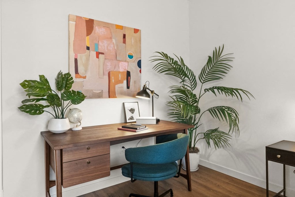 A painting hangs on the wall above a desk with a chair and a plant at Cru at Willows Apartments, Redmond, Washington