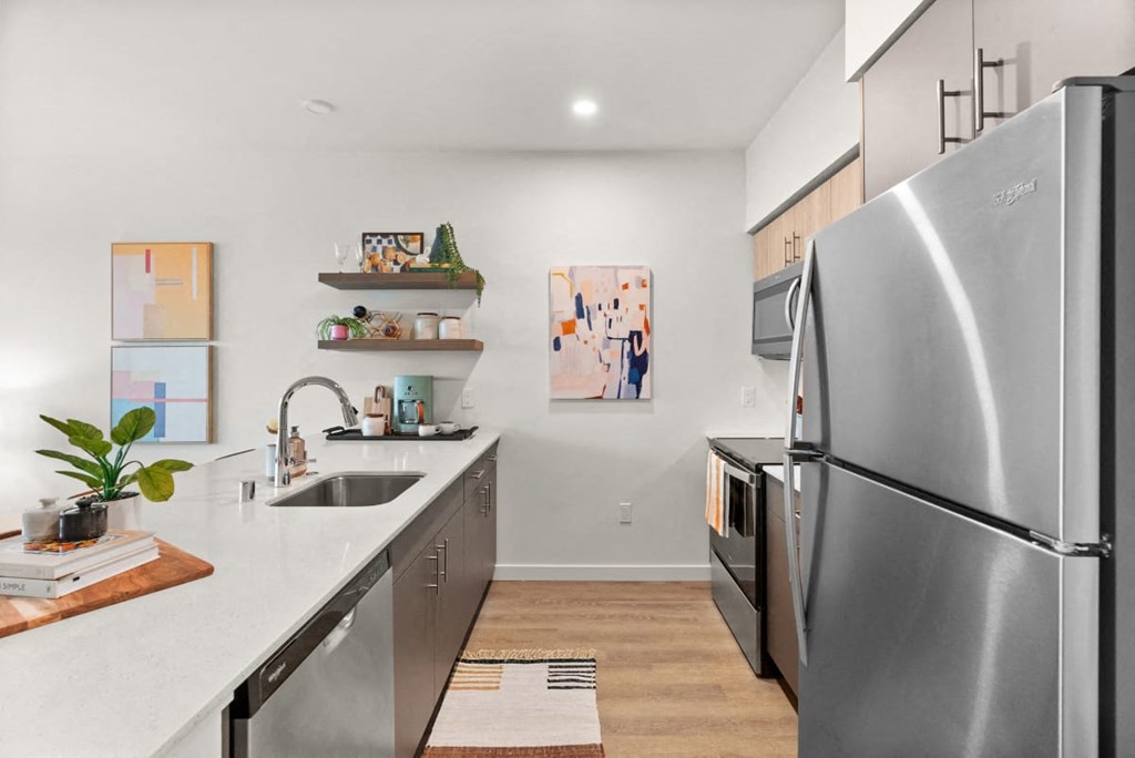 A modern kitchen with a stainless steel refrigerator and a sink with a plant on the counter at Cru at Willows Apartments, Redmond, 98052