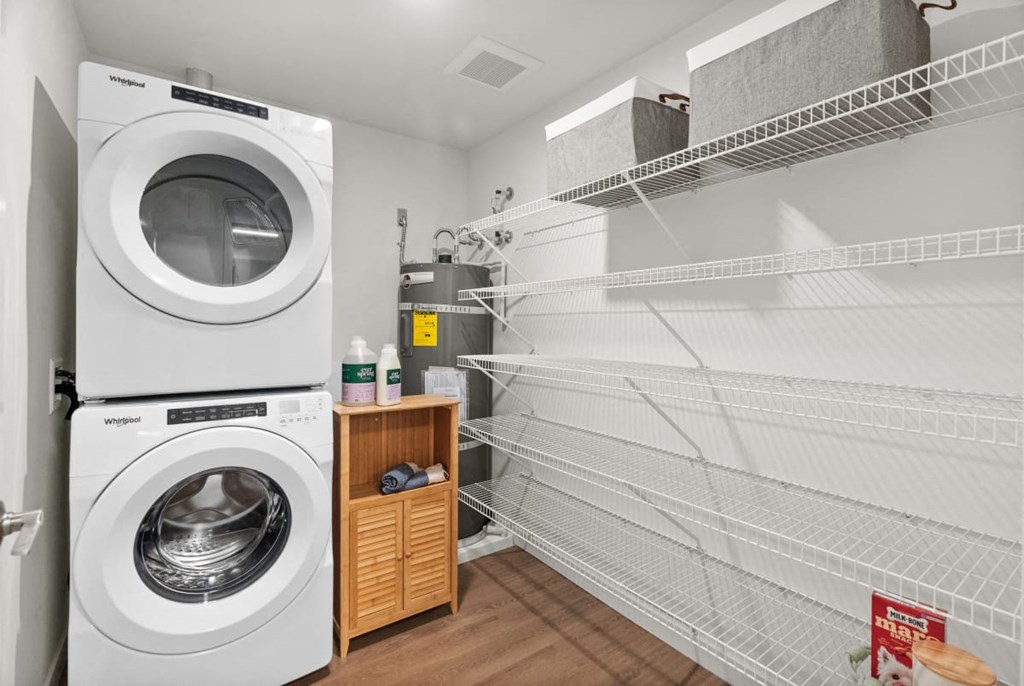 A white dryer is in a laundry room with a shelf and racks at Cru at Willows Apartments, Washington