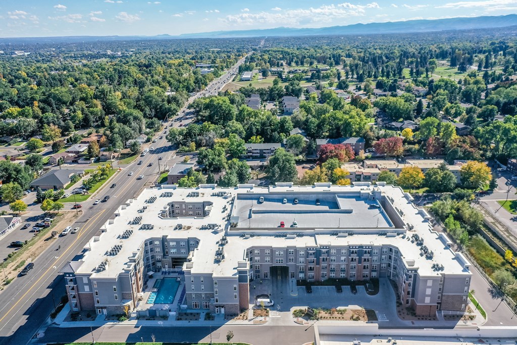 A large apartment complex with a swimming pool is surrounded by trees and roads.