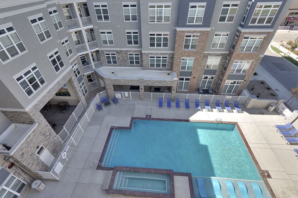 A large swimming pool is surrounded by a patio with lounge chairs and a stone building with a balcony.