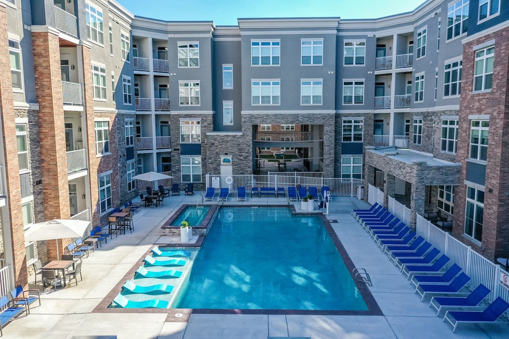 A large swimming pool surrounded by lounge chairs and umbrellas in a courtyard surrounded by apartment buildings.