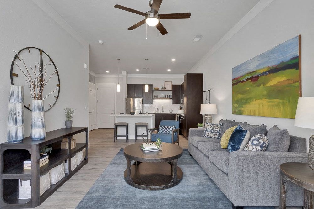 A living room with a grey couch, a coffee table, a bookshelf, and a painting on the wall.