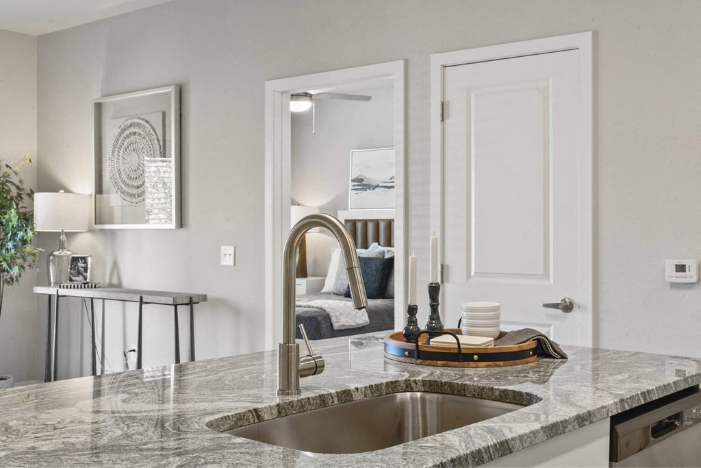 A modern kitchen with a marble countertop and a stainless steel sink.