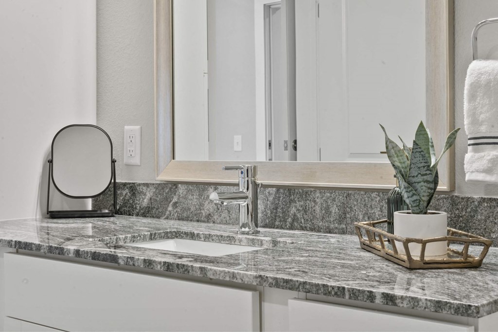 A bathroom counter with a marble top and a plant in a basket.