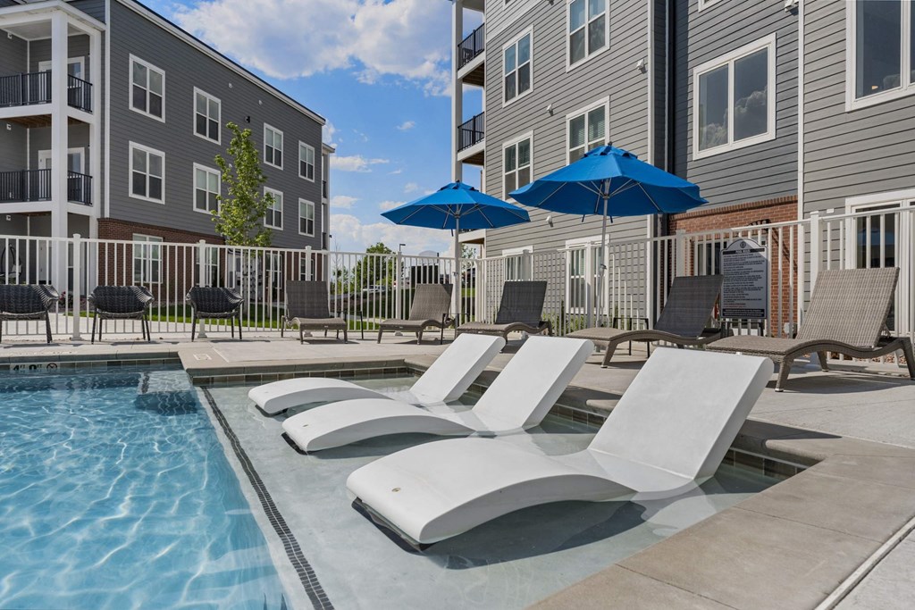 A pool with sun loungers and umbrellas in front of a building.