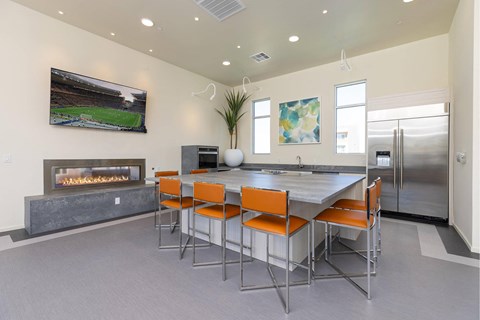 A modern kitchen with a fireplace and a dining table with orange chairs.