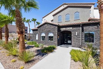A building with a stone facade and a sign that reads "LEASING CENTER" is surrounded by palm trees and landscaping.